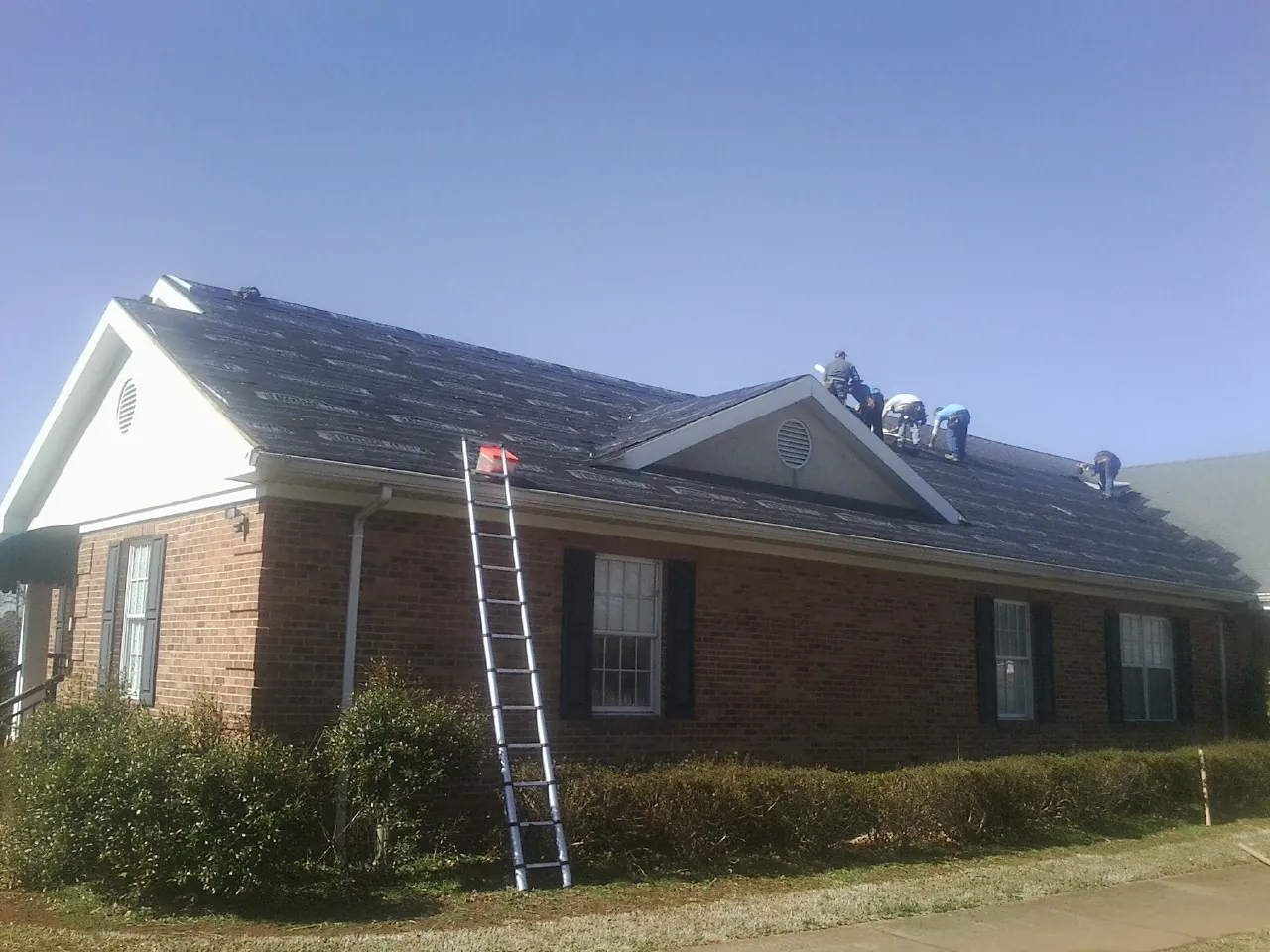 Crew tearing shingles off a brick ranch roof with a ladder set — Emergency Roof Repair work by our crew in Russiaville
