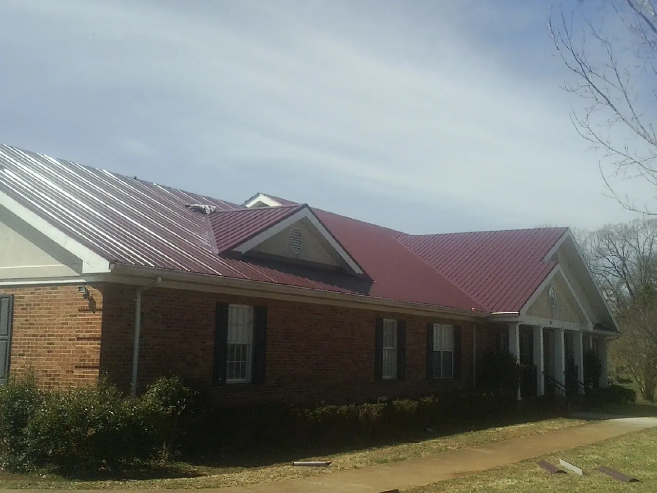 Red metal roof with gabled entries on a long brick building, from a Hail Damage Roof Repair job in Russiaville