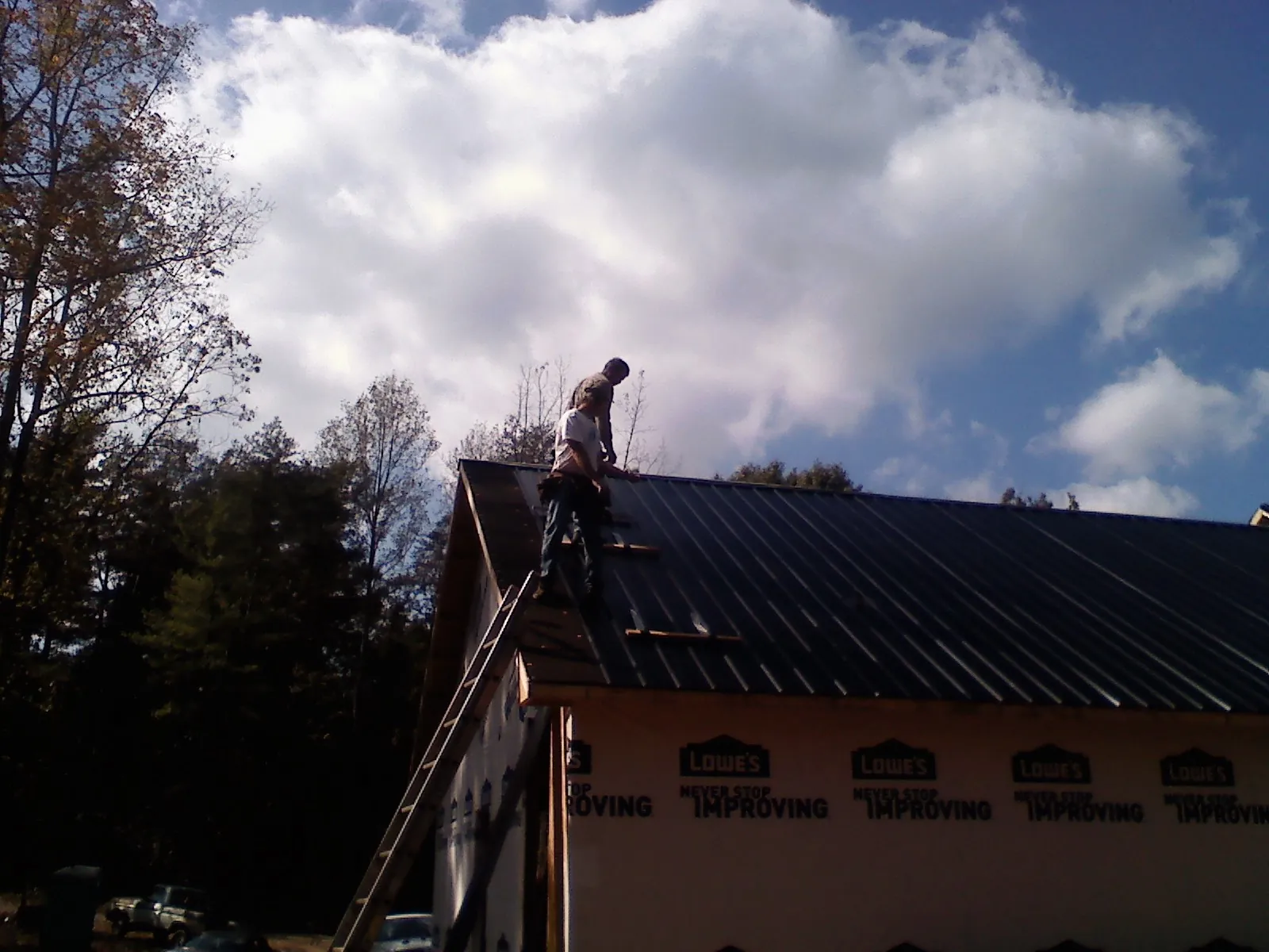 Roofer fastening dark metal panels high against a cloudy sky, from a Roof Inspection job in Russiaville