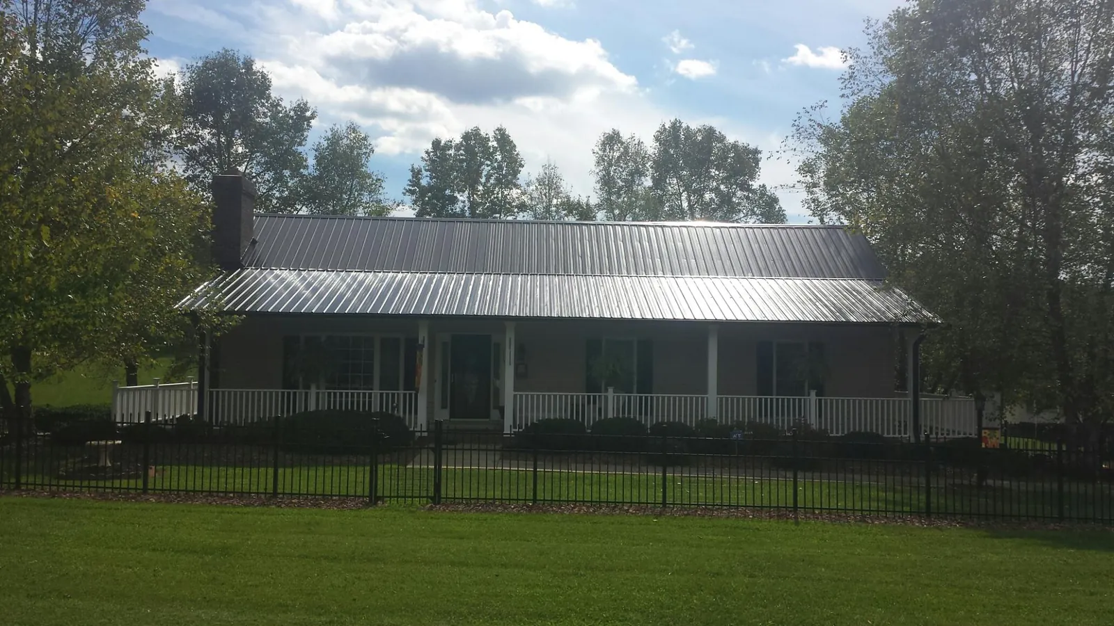 Gray metal roof on a brick ranch with a full width front porch — Gutter Guard Installation work by our crew in Russiaville