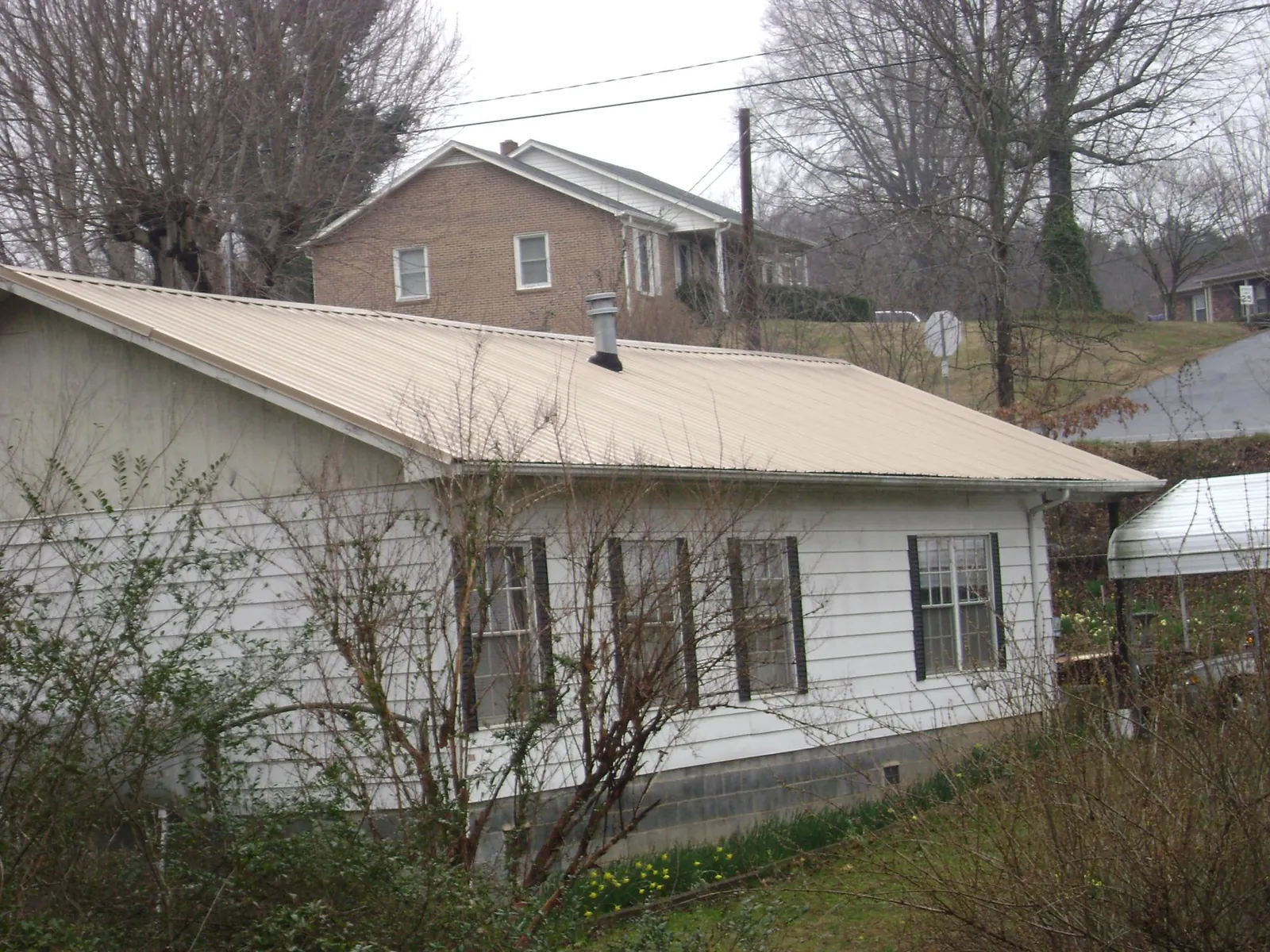 Tan metal roof on a white sided house set into a hillside — Commercial Roofing by Roofing Brothers in Russiaville