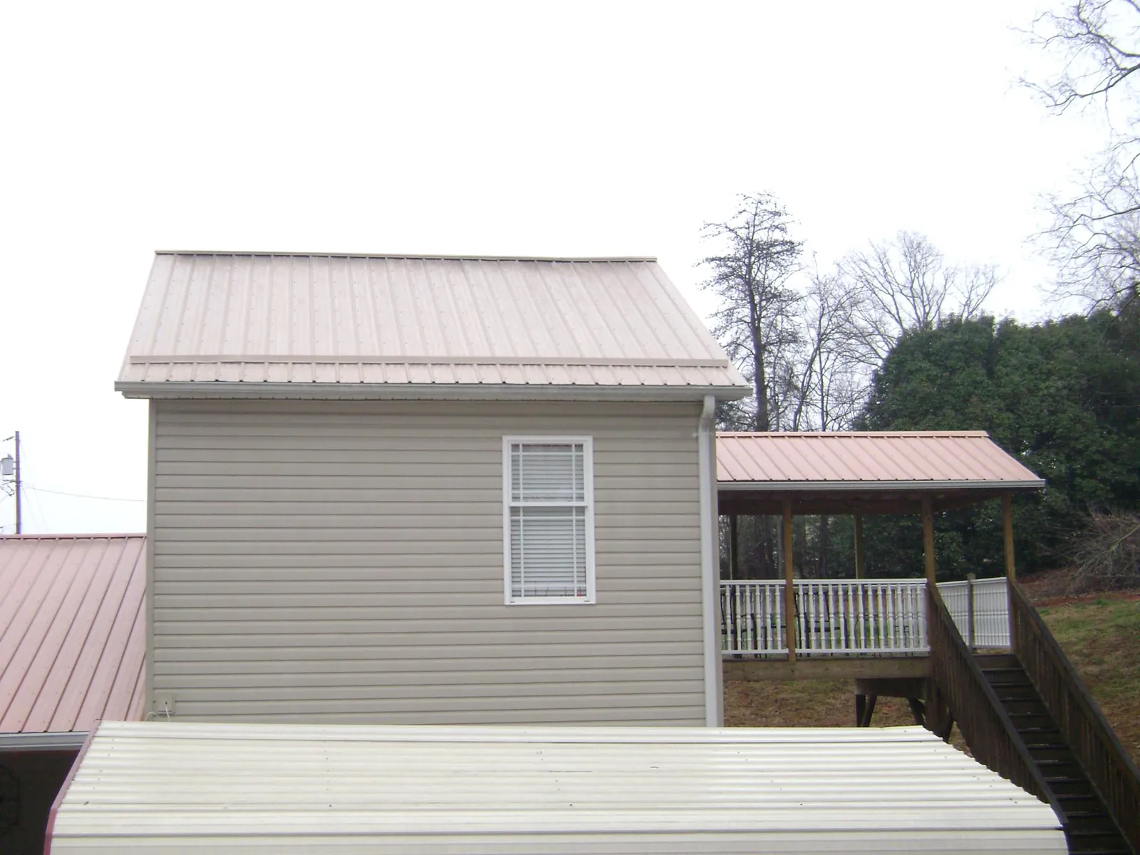 Tan metal roofs on a two story addition and attached porch, from a Roof Replacement job in Russiaville